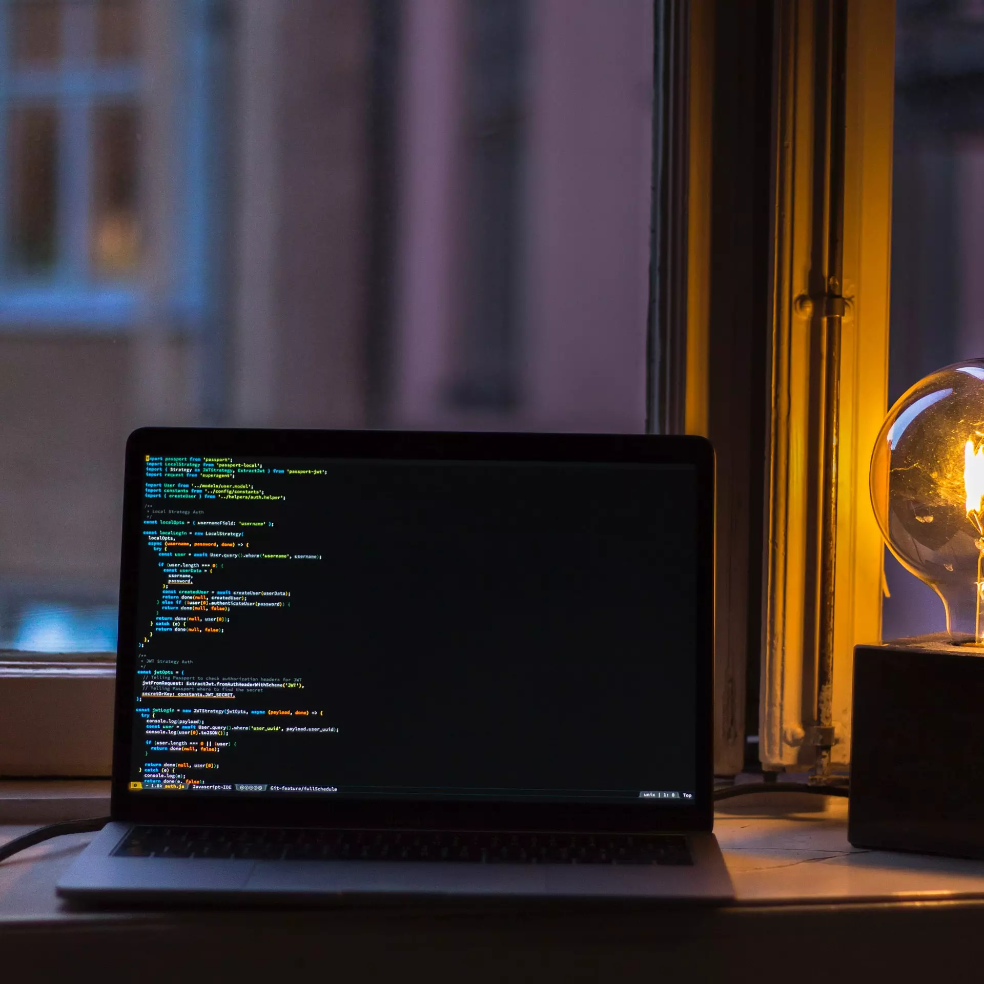 An image of code displayed on a laptop, with a lit lightbulb in the background.